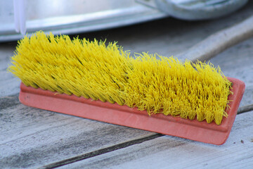A yellow broom with a red handle set on a wooden surface, with its bristles neatly arranged. The contrasting colors and textures add depth to the scene	
