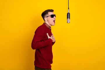 Cheerful Young Man Singing Into Microphone Against Bright Yellow Background in Stylish Attire