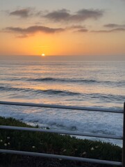 A vertical portrait of a stunning sunset over the ocean in La Jolla, California, featuring a rustic fence against the vivid sky.