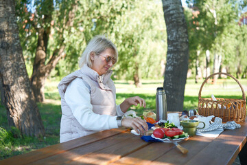 A young woman is savoring a pleasant and serene outdoor picnic that is pleasantly surrounded by...