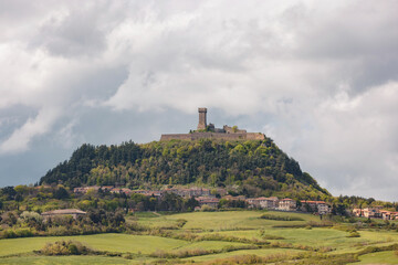 A historic castle is perched atop a lush green hill, surrounded by scenic rural landscapes. The sky...