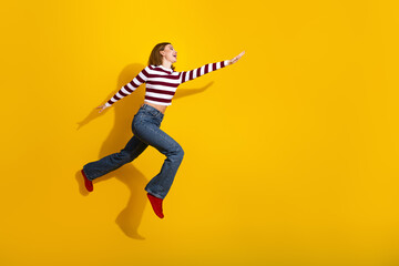 Trendy young woman in a striped pullover jumping gracefully against a bright yellow background with...
