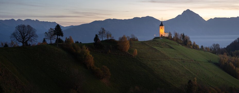 Landscape with small church on top of a hill and mountains in backdrop during sunrise, Slovenia, EU