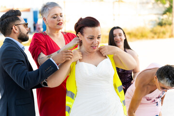Friends helping bride wearing high-visibility vest on roadside