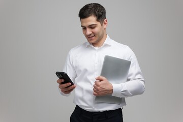 Young professional engaging with smartphone while holding laptop in casual office setting