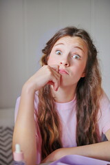 Girl with charming expression resting her chin on her hand while sitting in a cozy, well-lit room...