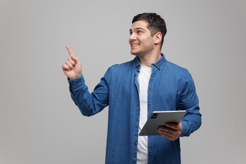 Joyful young man engaged in creative thinking while holding a tablet in a minimalistic studio...