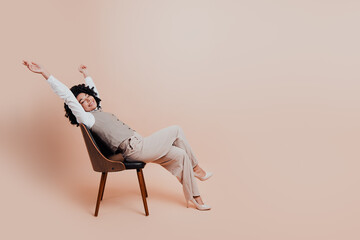 Young professional businesswoman in formal attire stretching and relaxing on a beige background...