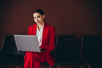 Confident Businesswoman in Elegant Red Suit Using Laptop Against Stylish Brown Background