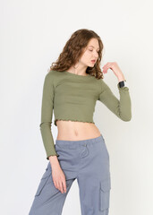 A stylish curly-haired woman dressed in a sporty style of clothes poses on a white background