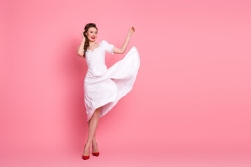 Elegant young woman in white dress smiling and posing gracefully against a pink background in a...