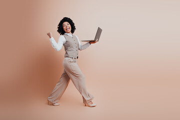 Confident businesswoman walking with a laptop, expressing joy and success against a stylish modern...
