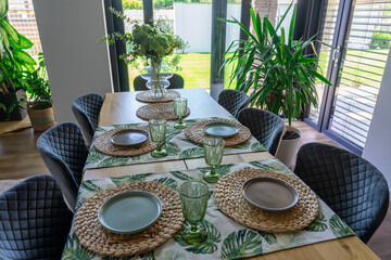 Stylish indoor dining area illuminated by sunlight through large windows, adorned with green plants and tasteful tableware emphasizing eco-inspired contemporary interior design and natural elements