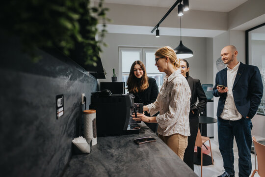 A group of business colleagues gather around a coffee maker, sharing smiles and conversation during a break in a modern, well-lit office space.