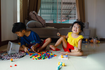 Happy adorable kindergarten boy and girl enjoying play toy block building in cozy house