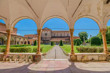  Ferrara, Italy - May 17, 2025: Saint Christopher church of Charterhouse of Ferrara, framed by arches of the cloister, with green lawn, bushes and blue sky, in a sunny summer day in Ferrara, Italy