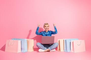 Young woman celebrates online shopping success surrounded by pastel shopping bags on a vibrant pink...