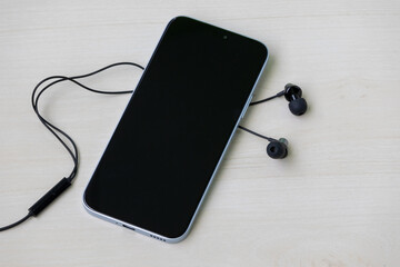 Smartphone and wired black earphones on light wooden surface.