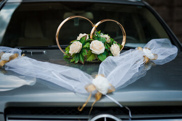 Wedding car decoration with gold rings and white flowers on the hood, draped with sheer white fabric, symbolizing love.