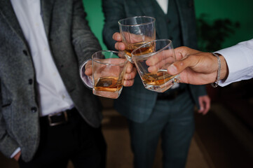 Three well-dressed men in suits raising glasses of whiskey in a celebratory toast during an elegant gathering, possibly a wedding or business event.