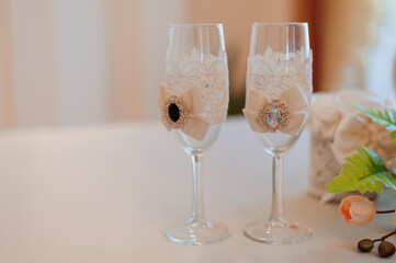 Elegant wedding toasting glasses adorned with delicate lace and peach ribbons, featuring jeweled accents, displayed on a white table setting