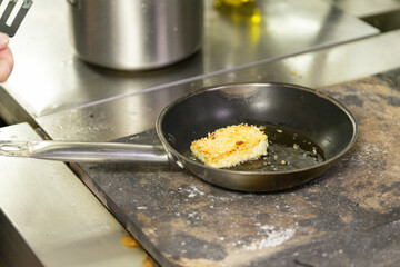 Breaded tofu frying in pan on stove with oil drizzle
