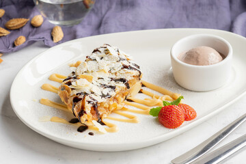 Delicious almond chocolate strudel dessert with ice cream and strawberries on white plate