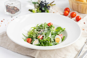 Fresh arugula salad with cherry tomatoes and quail eggs on white plate