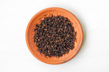 Clay plate of dried cloves (Syzygium aromaticum) on white. Top view of aromatic spice.