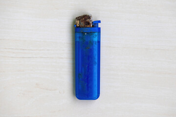 Old blue gas lighter, rusted, on light wood surface, top view.