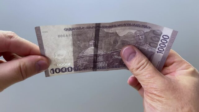 Horizontal 4K video. Male hand with cash money of Armenia. Man checking watermark with portrait of composer Komitas Soghomonian and lyre sign on 10000 dram bank note. Bribe, tax, debt, pay loan. Bill
