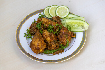 Delicious Irani Chicken Karahi or Kadai Bhuna Curry on white plate wooden background. Tasty hot spicy Iranian chicken Kadhai garnished with coriander, cucumber, lemon.