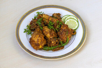 Delicious Irani Chicken Karahi Bhuna Curry on white plate, wooden background. Tasty hot spicy Iranian Kadai garnished with coriander and lemon.