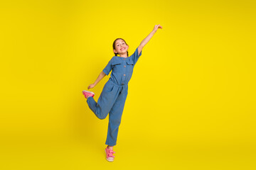 Cheerful young girl posing in blue outfit on vibrant yellow background, expressing joy, happiness,...