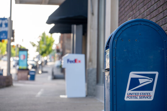 Sioux Falls, South Dakota, USA - 5.15.2025: Selective focus on a USPS mailbox with a defocused FedEx mailbox in the distance.
