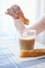 Madrid typical breakfast, unrecognizable woman having a coffee with milk while dipping golden,...
