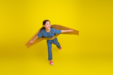 Happy young girl playing with cardboard wings, expressing creativity and imagination against a...