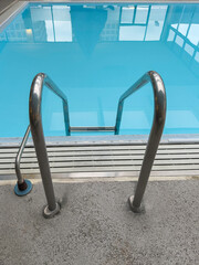 High-angle view of a pool ladder for stepping into or out of a reflective swimming pool inside a hotel. Motifs of hospitality and safety, recreation and fitness.