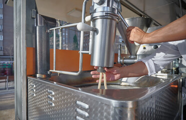 unidentified man is frying churros at a street-side churro shop, utilizing a professional dispenser machine. Traditional methods in a modern urban setting
