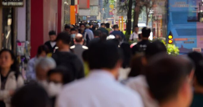 Overhead defocused view of crowded Nathan Road sidewalk in Hong Kong, filled with walking pedestrians along its entire visible length. This motion emphasizes busy city rhythm