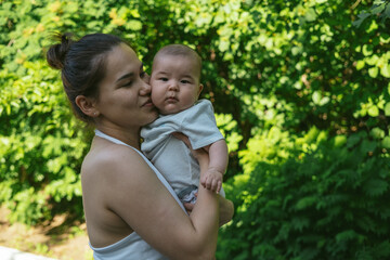 Young Asian mother is holding cute boy son and kissing his cheeks with love and tenderness. Newborn baby cute and cheerful. Concept of motherhood parenting. 