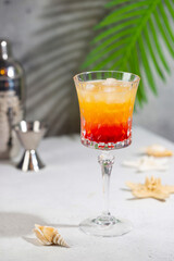 Colourful exotic Tequila Sunrise cocktail in a glass served with ice on gray background