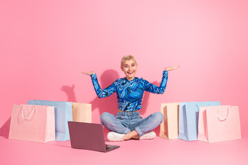 Young woman with short blonde hair sitting surrounded by shopping bags, happily gesturing amidst a...