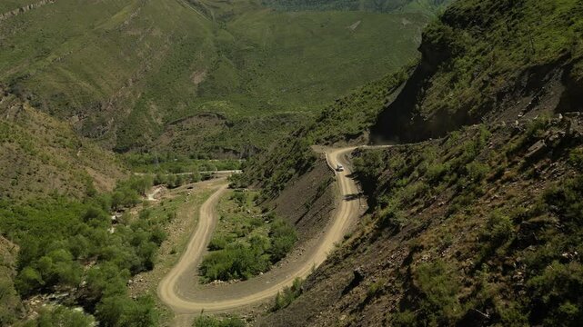 Dron video road in mountains. Drone flying over a car driving on a serpentine road in the mountains SUV. Green fields and impressive top view