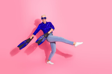 Cheerful senior woman in casual blue shirt and flippers posing on a vibrant pink background exuding confidence and positivity