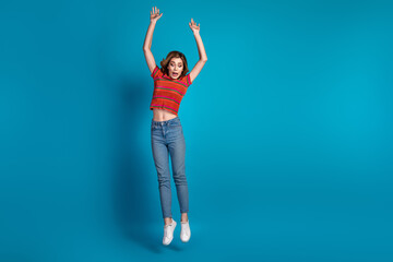 Plakat Cheerful young woman in stylish outfit jumping joyfully against bright blue background