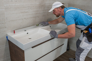 Installation of bathroom furniture. A worker measures the horizontality of a bathroom sink and...
