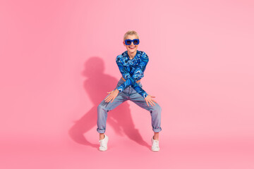 Young woman in trendy blue top and sunglasses posing playfully against a pink background showcasing modern fashion