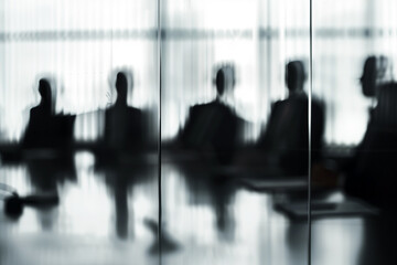 An abstract image of a business meeting as seen through a window, featuring blurred figures seated around a table. Suggests collaboration, strategic planning, and teamwork in a corporate setting.