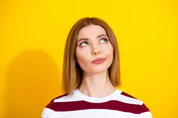 Thoughtful young woman gazing upward over a vivid yellow background wearing a stylish striped...